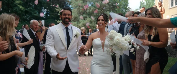 A bride and groom walking down the aisle at a wedding, surrounded by guests and falling petals.