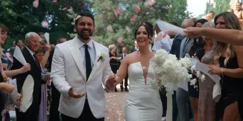 A bride and groom walking down the aisle at a wedding, surrounded by guests and falling petals.
