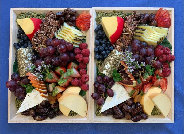 Two wooden platters filled with an assortment of cheeses, fresh fruits, nuts, and dried fruits.