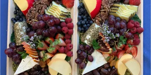 Two wooden platters filled with an assortment of cheeses, fresh fruits, nuts, and dried fruits.