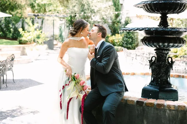 Bride and groom sharing a kiss beside a fountain at an outdoor wedding venue