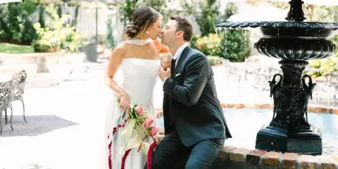 Bride and groom sharing a kiss beside a fountain at an outdoor wedding venue