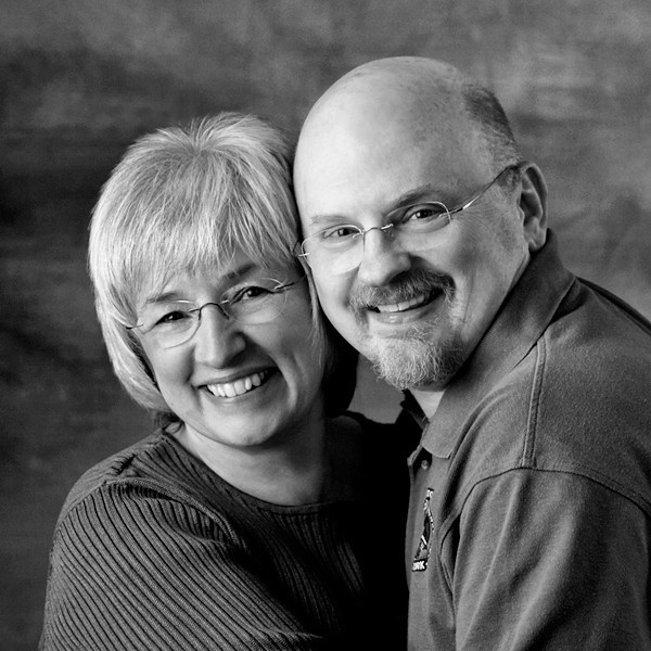 A black and white portrait of a smiling woman and man, identified as the photographers Sharon and Greg Lewis.