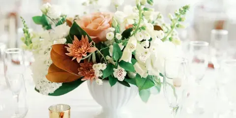 A floral centerpiece featuring white and peach flowers in a white vase on a table setting.