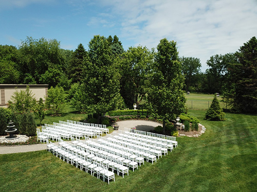 An outdoor garden wedding venue with rows of white chairs set up for a ceremony, featuring a fountain and lush greenery.