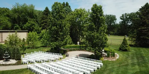 An outdoor garden wedding venue with rows of white chairs set up for a ceremony, featuring a fountain and lush greenery.