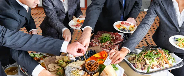 Catering staff serving a buffet of charcuterie, fruit, and salad platters to guests.