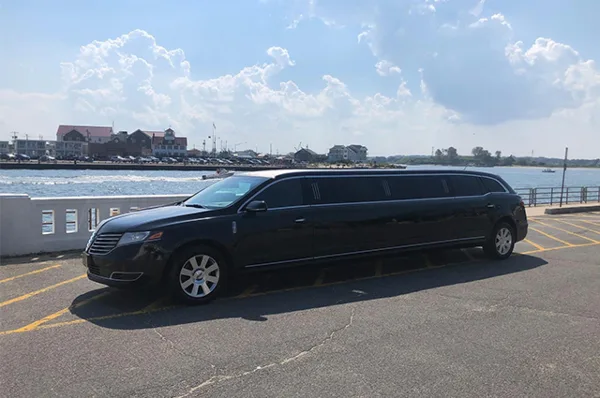 A black stretch limousine parked in a lot near a body of water.