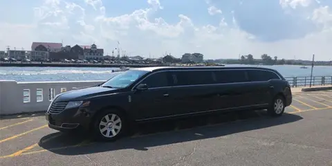 A black stretch limousine parked in a lot near a body of water.
