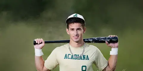 A young man in an Acadiana baseball uniform holding a signed bat, with a Dubois Images watermark.