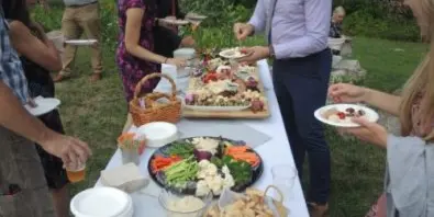 Guests serving themselves from an outdoor buffet table featuring vegetables, dips, and appetizers.