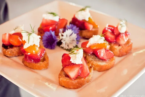 A plate of gourmet canapés topped with fresh fruit, cream, and herbs, garnished with edible flowers.
