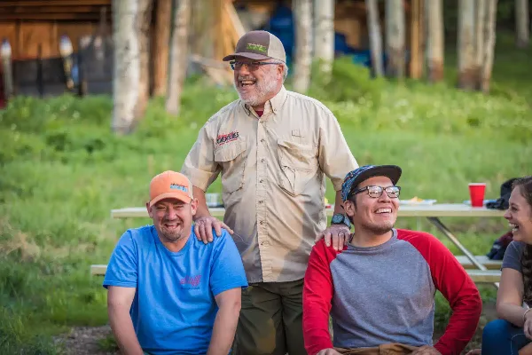 A group of smiling people, including a guide in a Blazing Adventures uniform, sitting outdoors at a picnic table.