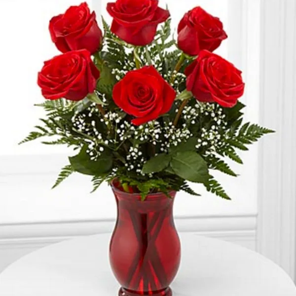 A bouquet of red roses with greenery and baby's breath in a red glass vase.