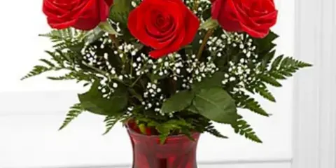 A bouquet of red roses with greenery and baby's breath in a red glass vase.