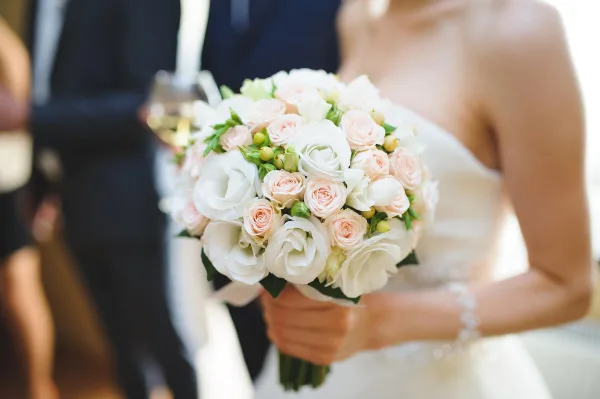 A close-up of a bride holding a round bouquet of white and blush roses with green accents.