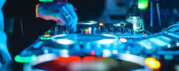 A close-up view of a DJ's hands adjusting controls on a professional audio mixer and turntable setup.