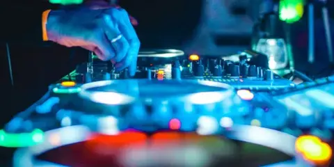 A close-up view of a DJ's hands adjusting controls on a professional audio mixer and turntable setup.