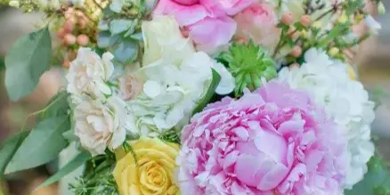 A close-up of a bride holding a bouquet of pink peonies, white roses, and greenery.