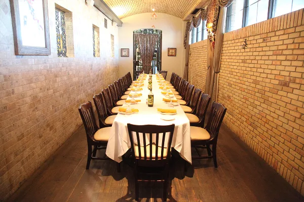 A long banquet table set with white linens and place settings in a room with exposed brick walls.