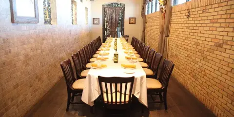 A long banquet table set with white linens and place settings in a room with exposed brick walls.