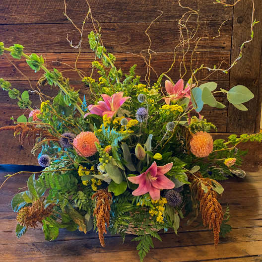 A large mixed floral arrangement featuring pink lilies, peach dahlias, and greenery in a basket.