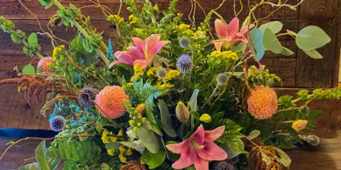 A large mixed floral arrangement featuring pink lilies, peach dahlias, and greenery in a basket.