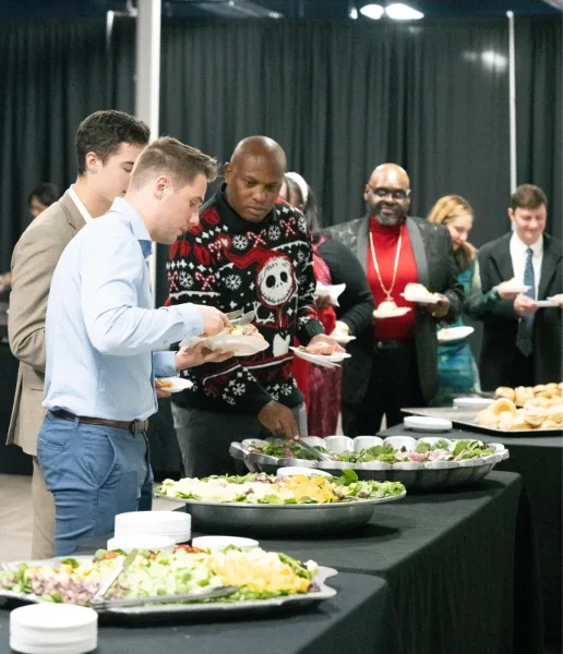 Guests serving themselves from a buffet table with various food trays at a catering event.
