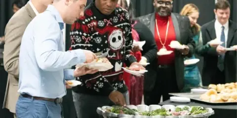 Guests serving themselves from a buffet table with various food trays at a catering event.