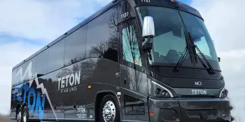 A black Teton Stage Lines charter bus parked outdoors.