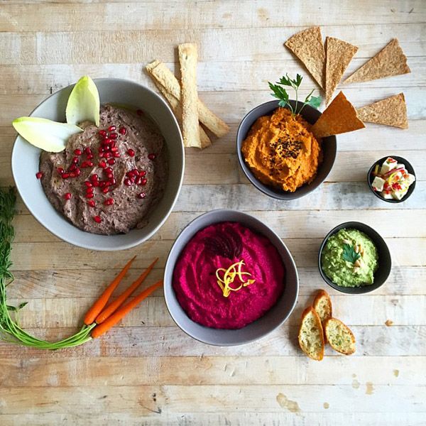 An overhead view of various catering appetizers, including hummus, dips, and fresh vegetables, arranged on a wooden table.