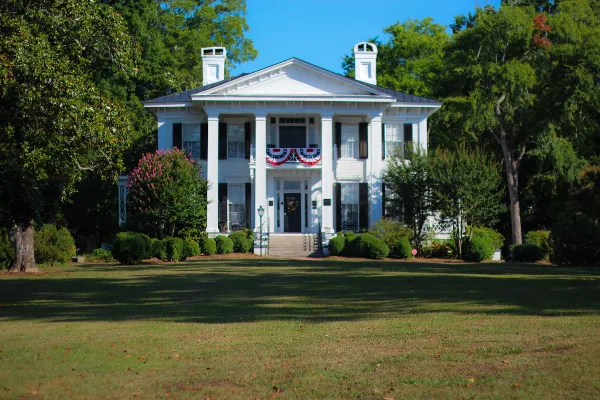 Exterior view of the white Burt-Stark Mansion with a large lawn and surrounding trees.