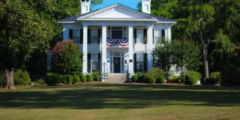Exterior view of the white Burt-Stark Mansion with a large lawn and surrounding trees.