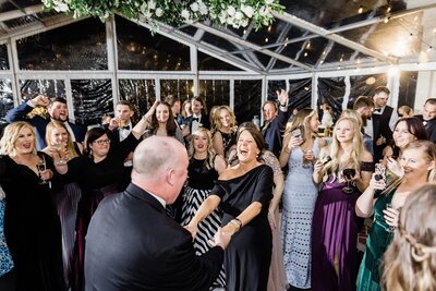 A DJ at a wedding reception interacting with a crowd of guests on a dance floor.