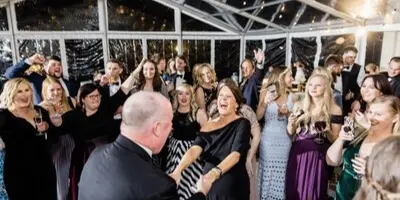 A DJ at a wedding reception interacting with a crowd of guests on a dance floor.