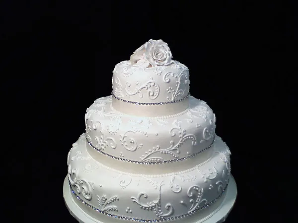 A three-tiered white wedding cake decorated with floral piping and a rose topper.