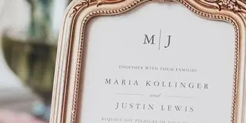 A close-up of a wedding invitation in an ornate gold frame, listing Barn at the Bluff in Woodbine, Georgia as the venue.