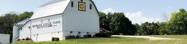 Exterior view of the white Elmore Stock Farm barn building with a quilt pattern on the roof and a gravel driveway.