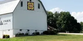 Exterior view of the white Elmore Stock Farm barn building with a quilt pattern on the roof and a gravel driveway.
