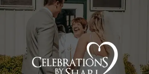 A wedding officiant in white robes smiling while standing between a bride and groom during a ceremony.
