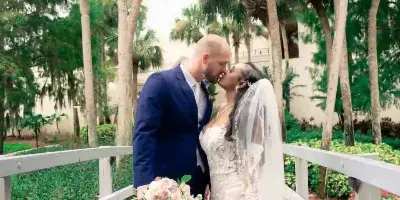 A bride and groom kissing on a wooden bridge surrounded by palm trees.