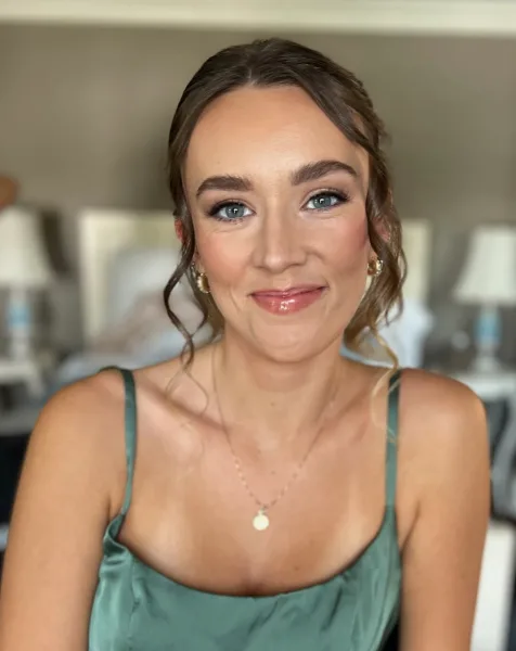 Bride with styled hair and full makeup facing the camera in a bedroom setting