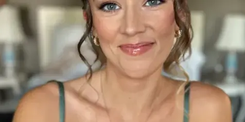 Bride with styled hair and full makeup facing the camera in a bedroom setting