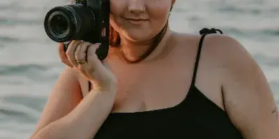 Portrait of a female photographer with red hair holding a camera near a body of water.
