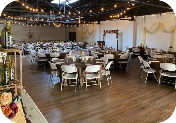 Interior view of a community hall event space with round tables, white chairs, and a floral archway.