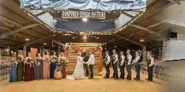 A wedding ceremony in progress inside a large, covered event hall with a stage and seating.