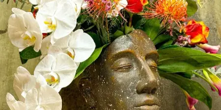 A vibrant floral arrangement with white orchids and orange proteas arranged in a sculptural head-shaped vase.