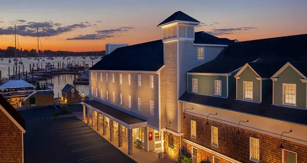 Exterior view of the Bristol Harbor Inn hotel building overlooking a harbor with boats at sunset.