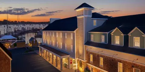 Exterior view of the Bristol Harbor Inn hotel building overlooking a harbor with boats at sunset.