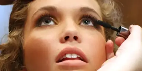 A close-up of a makeup artist applying mascara to a client's eye.